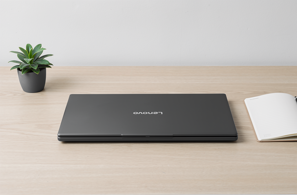 Ordinateur portable fermé sur un bureau épuré avec carnet et plante.